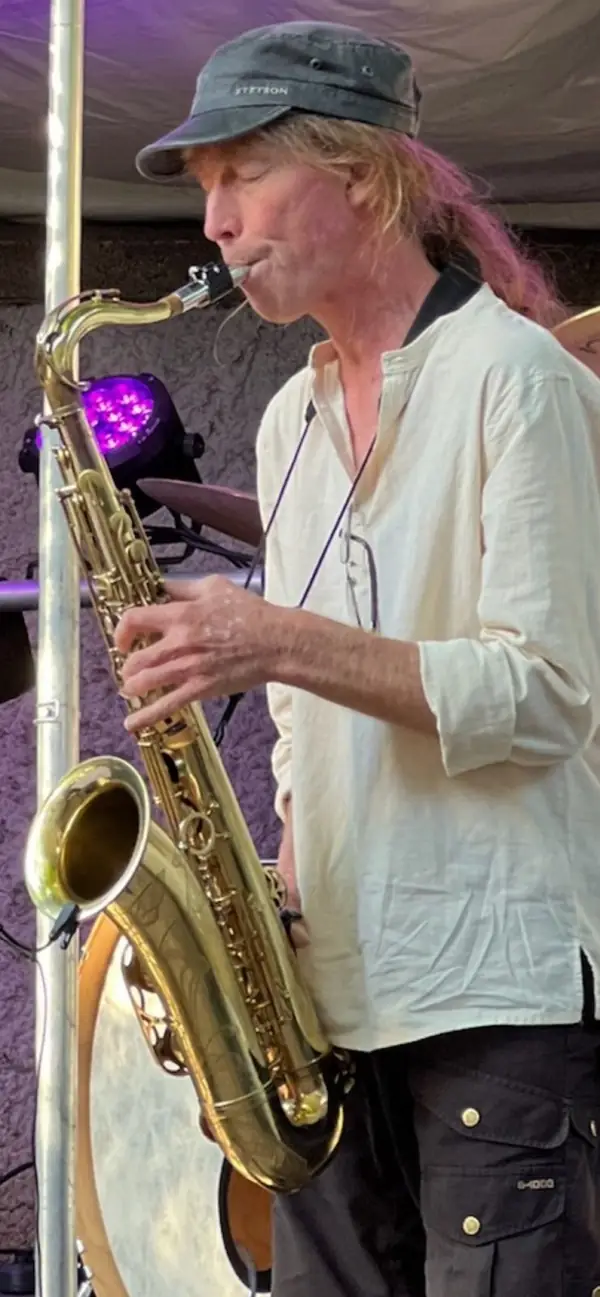 Dett Heidkamp mit Mütze am Tenorsaxophon bei einem Open-Air-Konzert im violetten Bühnenlicht