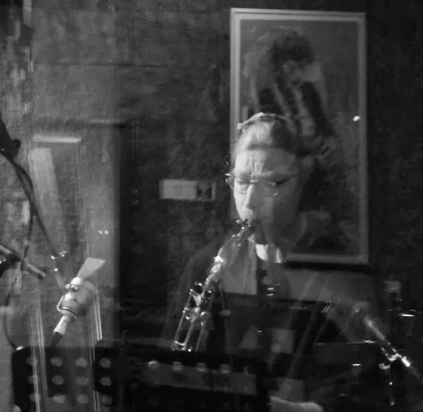Schwarzweißaufnahme: Dett Heidkamp am Saxophon hinter der Scheibe des Aufnahmeraums