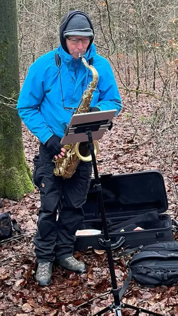 Dett Heidkamp übt im winterlichen Wald Saxophon, vor ihm ein Notenständer mit Tablet